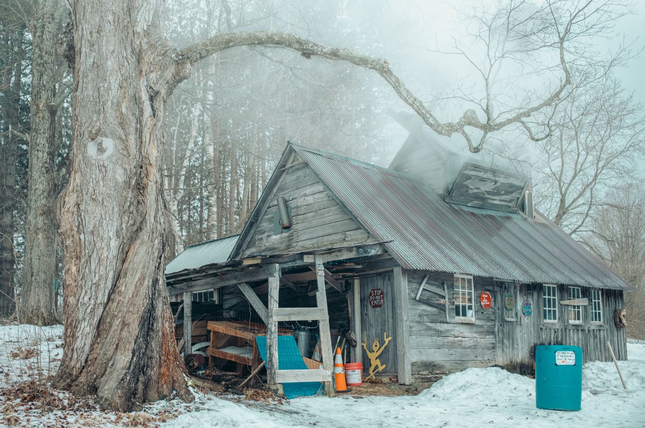 A weathered barn with steam coming out of its chimney.