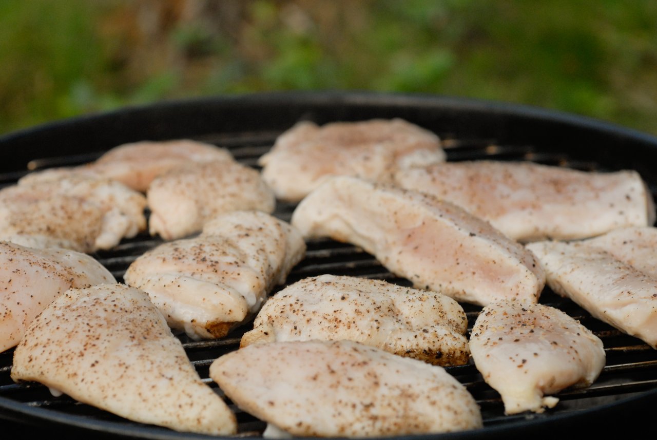 Seasoned chicken pieces cooking on a grill outdoors.