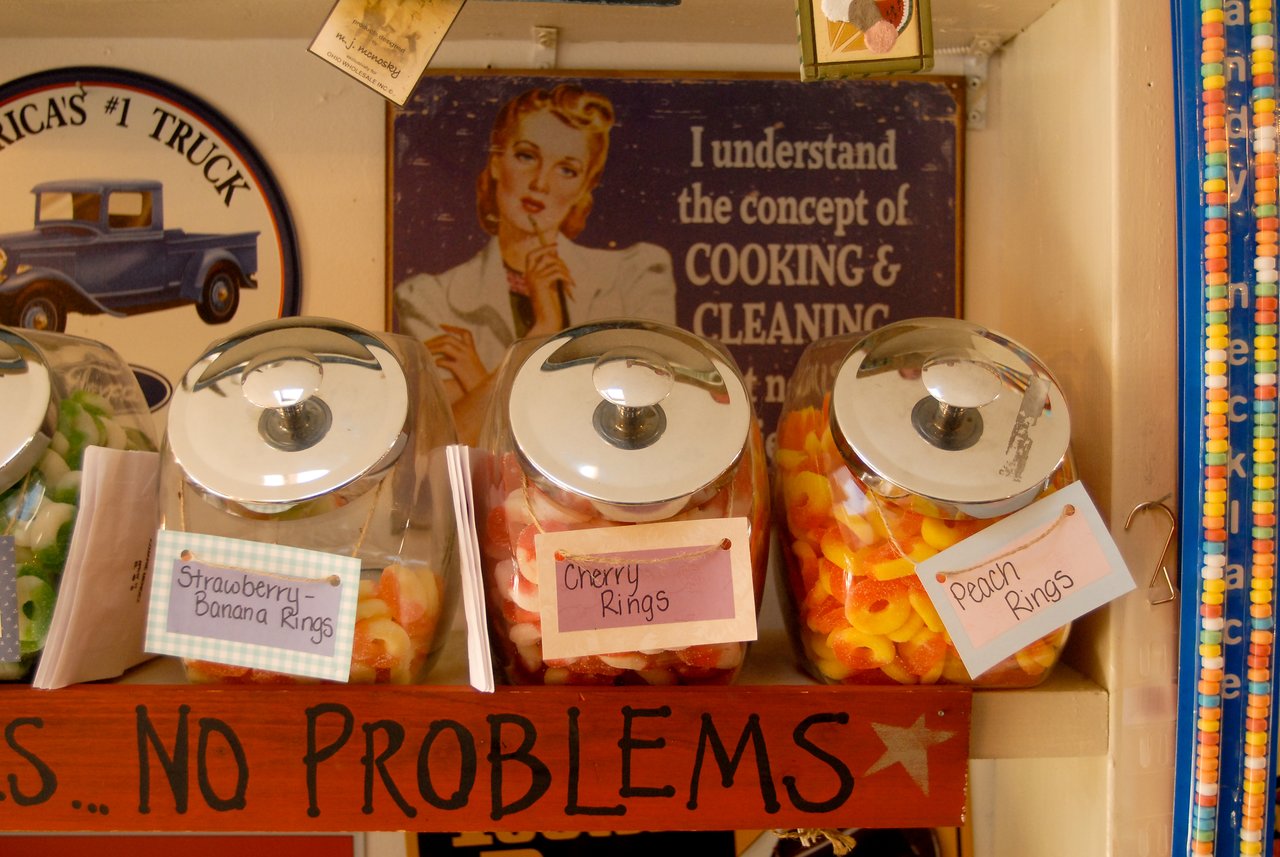 Glass jars filled with colorful gummy rings sit on a shelf, each labeled with different flavors like cherry and peach.