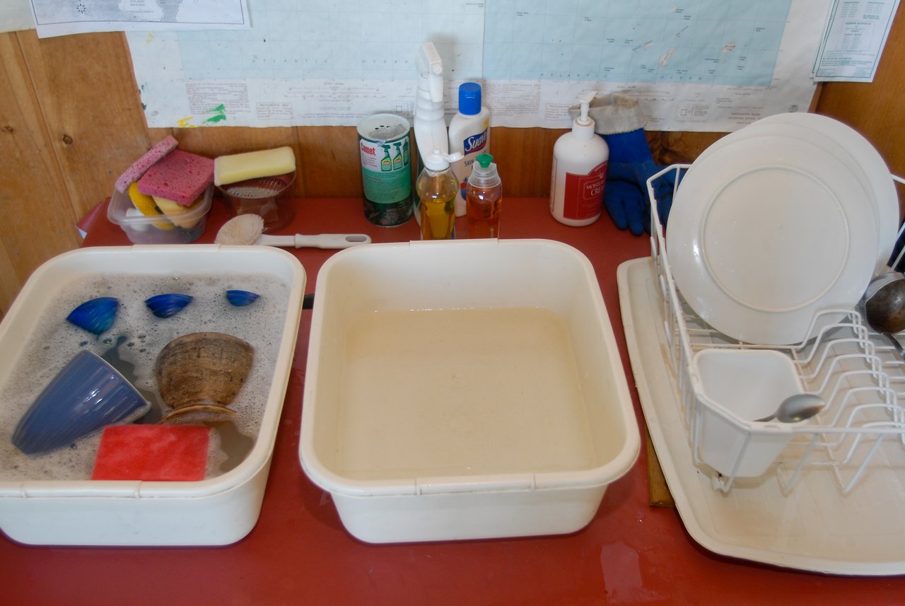 Two plastic basins filled with water for washing dishes, with clean dishes drying on a rack nearby.