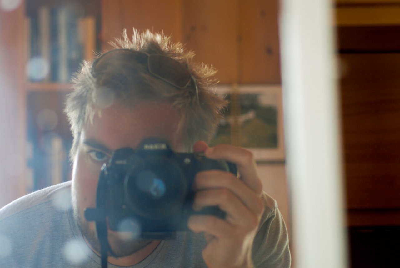 A person with messy hair takes a mirror selfie with a camera, partially hiding their face.