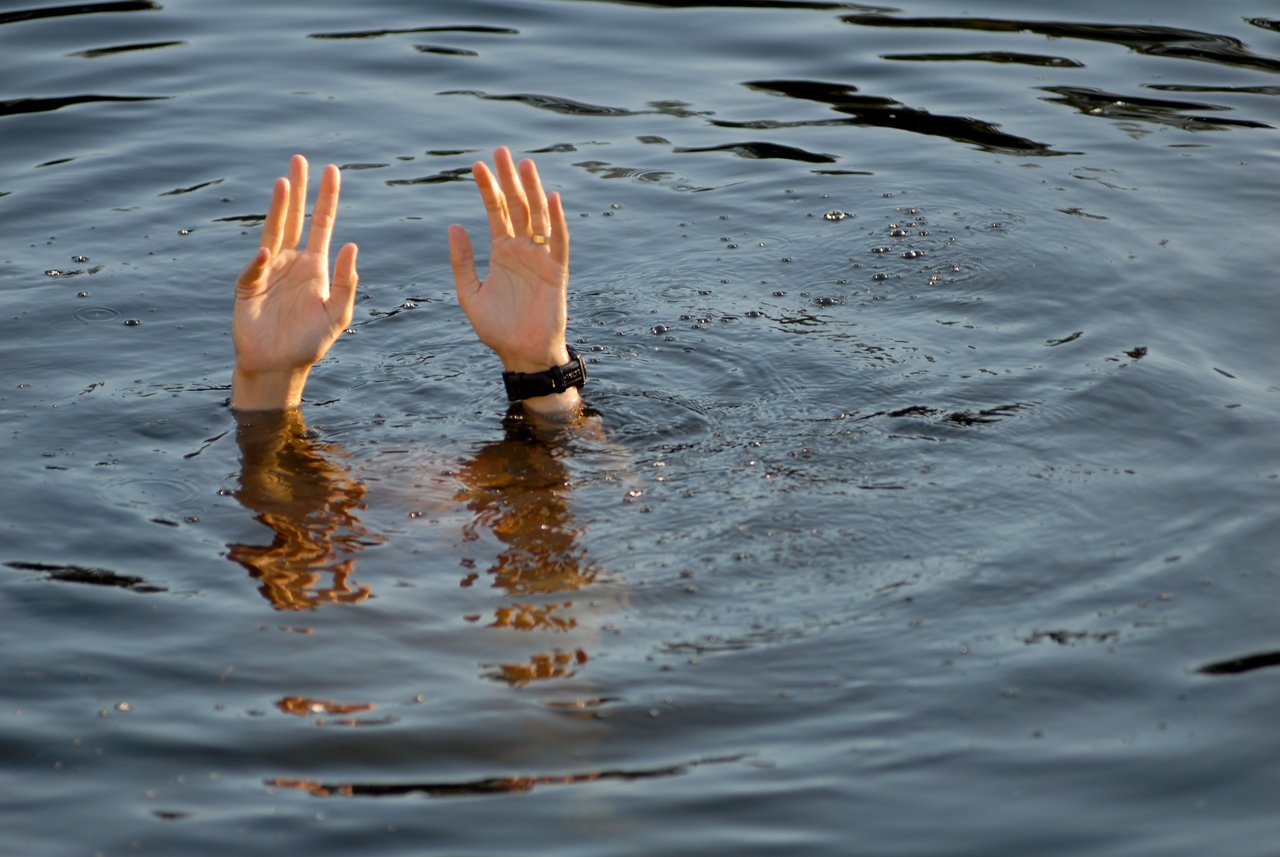 A person is partially submerged in water, with only their hands and wrists visible above the surface.
