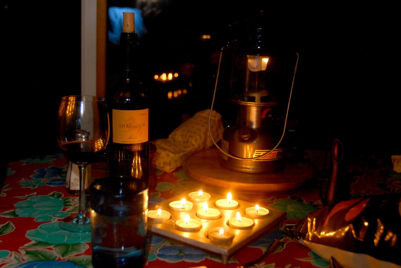 A table lit by candles and a lantern, with a bottle of wine, a glass, and other items.