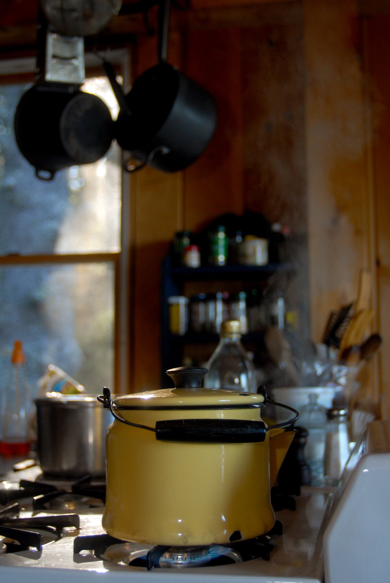 A yellow kettle is heating on a gas stove, with steam rising as water boils for coffee.