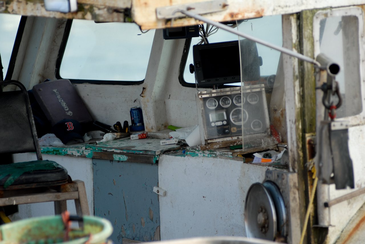 The interior of a working lobster boat, showing navigation equipment, tools, and personal items in a worn cabin.