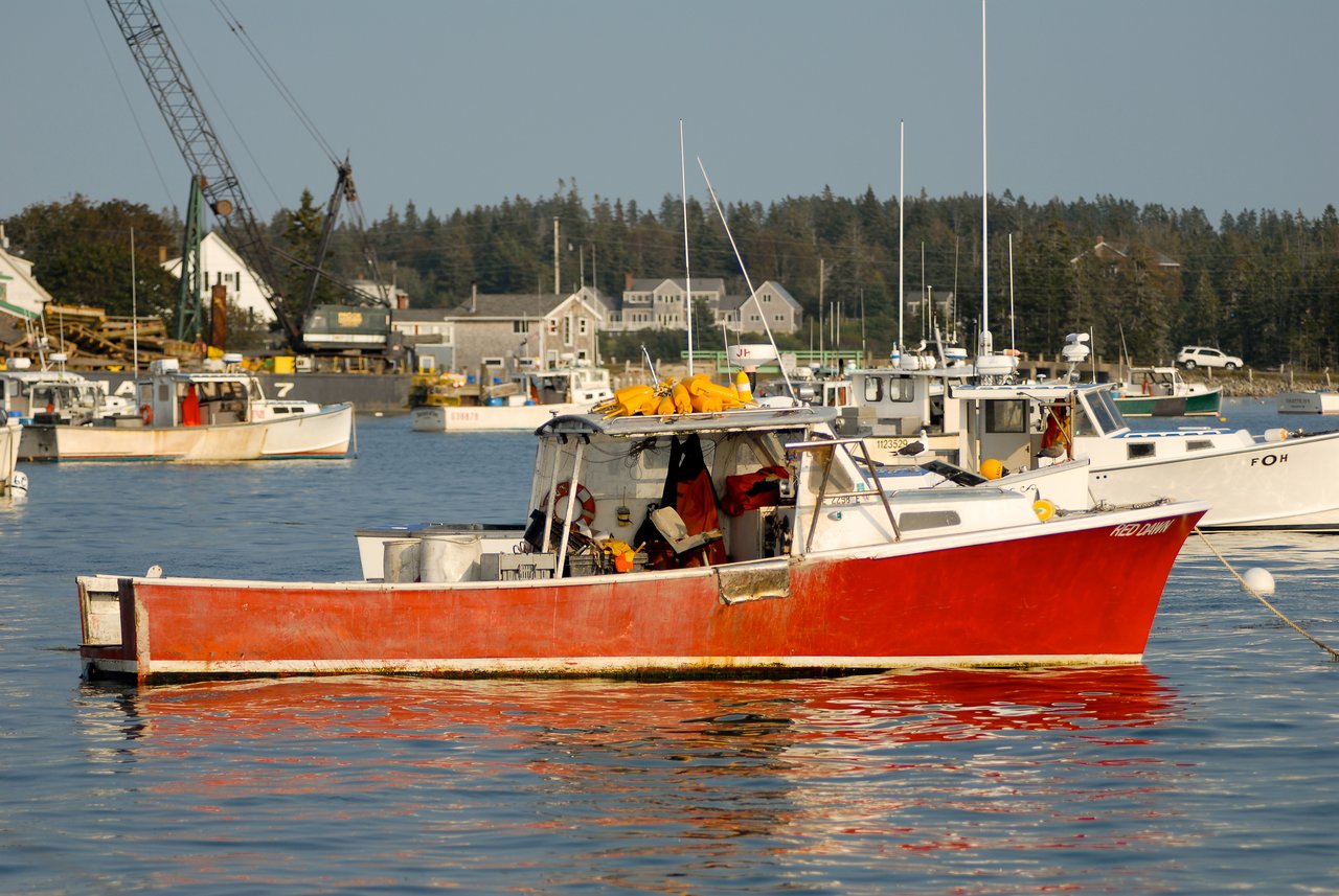 A red lobster boat floats in the harbor, loaded with fishing gear and equipment.
