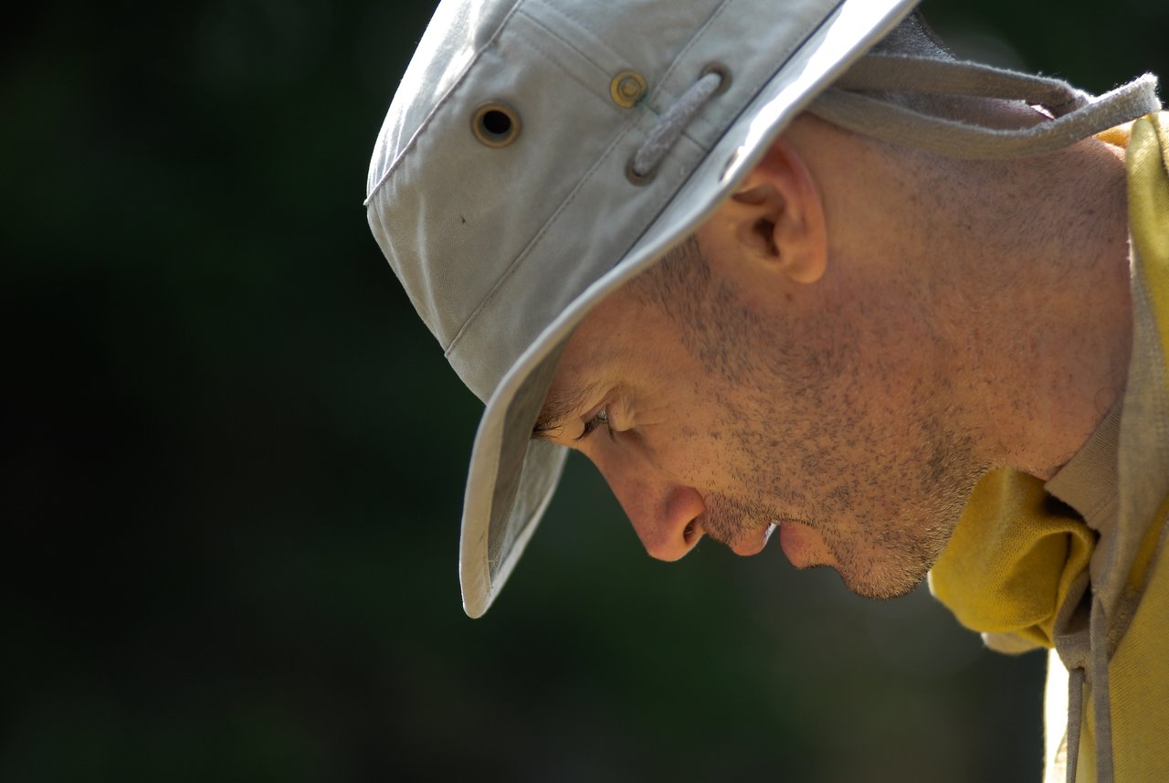 A person wearing a light-colored hat and yellow scarf looks downward with a focused expression.