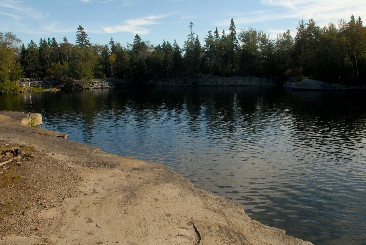 A calm quarry pond surrounded by trees, with a rocky shoreline in the foreground.