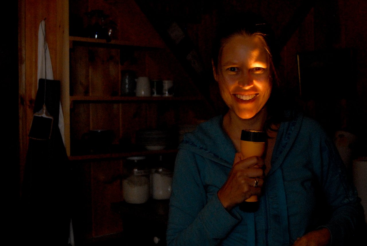 A woman in a dark room holds a flashlight under her face, creating a spooky lighting effect.