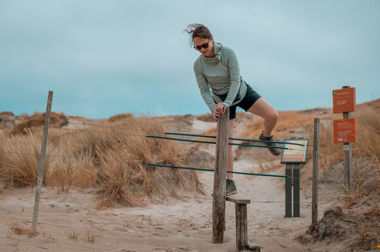 Vanessa standing on a step, with one leg raised in the air, as she climbs over an electric fence.