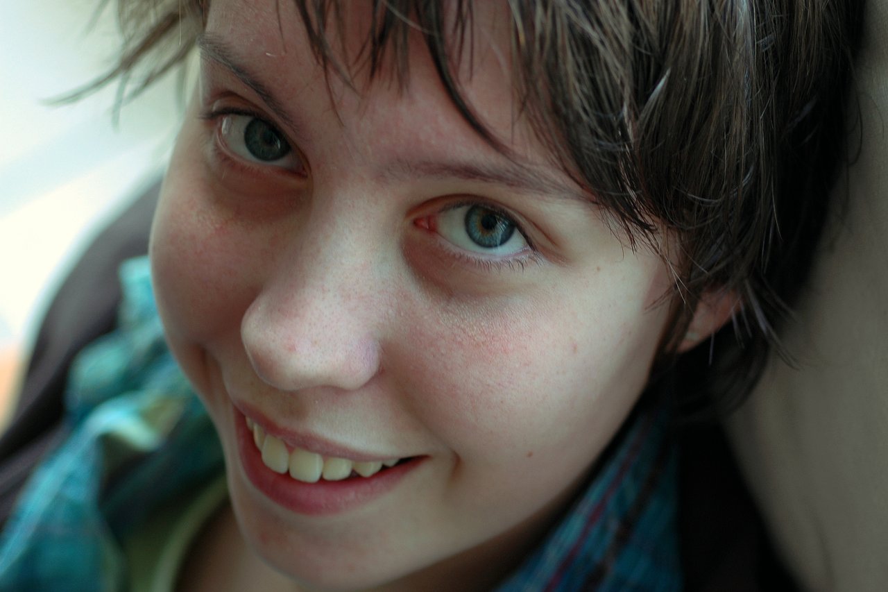 A person with short brown hair and blue eyes smiles while looking directly at the camera.