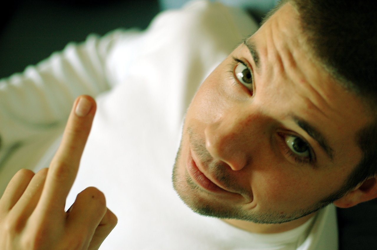 A person in a white shirt looks at the camera while raising their middle finger.