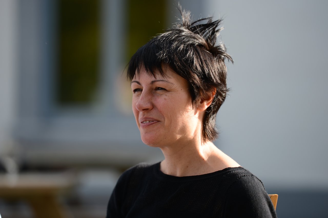 A woman with short black hair smiles while sitting outside during the day.