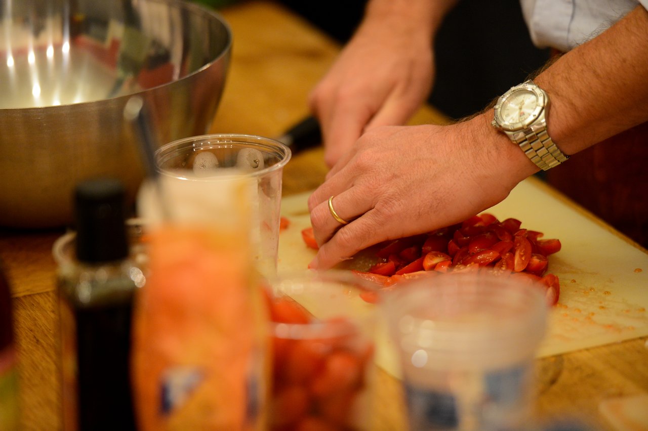 Close-up of hands chopping cherry tomatoes on a cutting board, with kitchen items and a mixing bowl nearby.