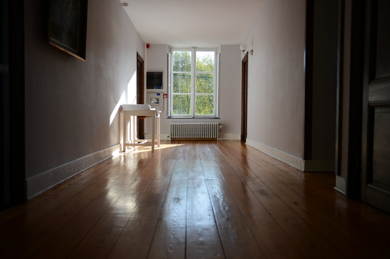 A quiet hallway with wooden floors, a small table, and a window letting in natural light.