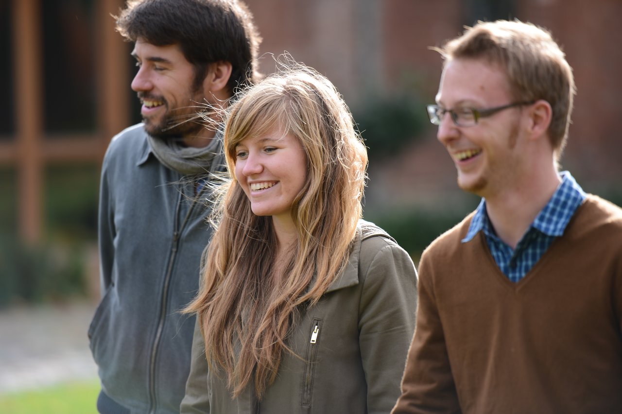 Three people walk outdoors, smiling and laughing together during a family weekend gathering.