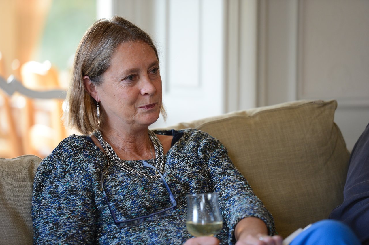 A woman sits on a couch, holding a glass of wine and engaged in conversation.