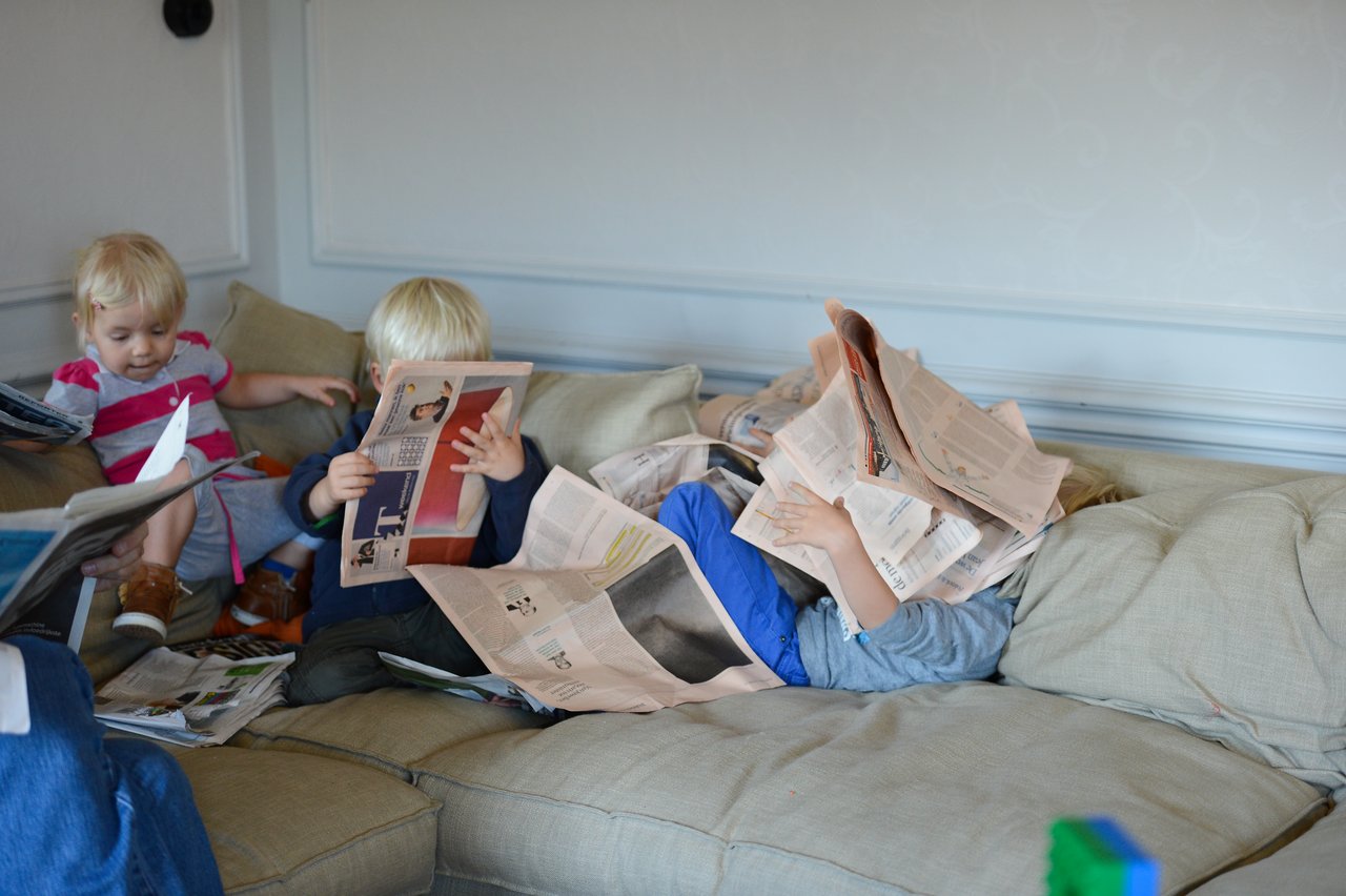 Children sitting on a couch, holding and playing with newspapers.