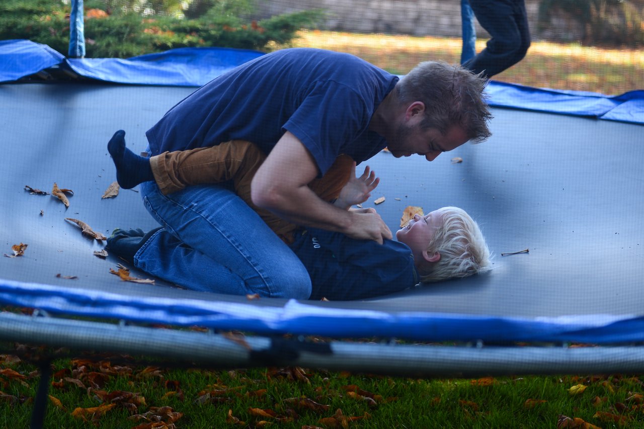 A man and a child laugh while playing together on a trampoline during a family weekend.