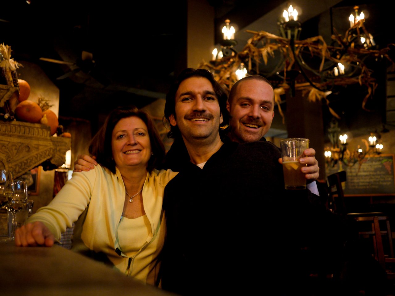 Three people smiling at a bar, with one holding a drink.