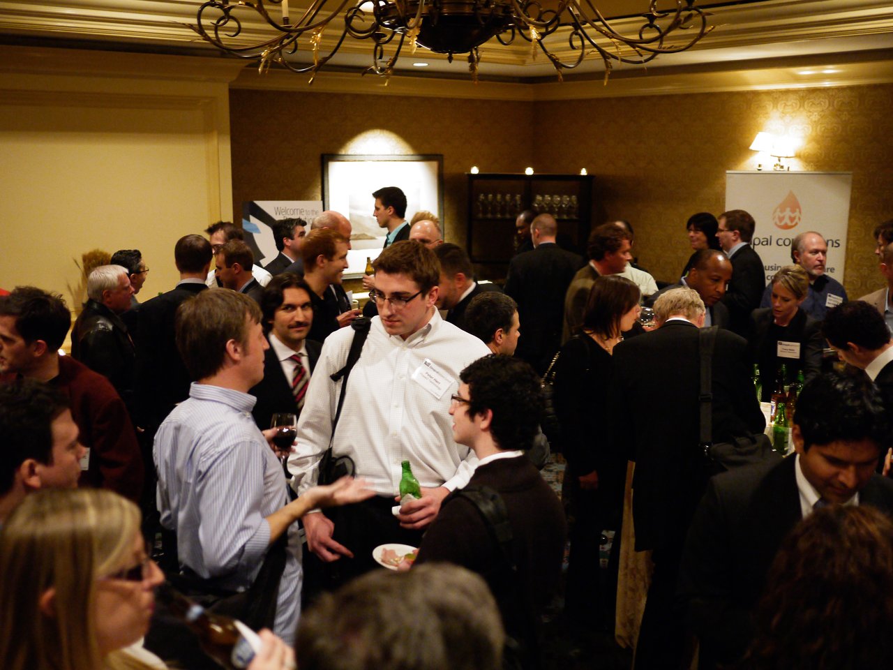 A crowded networking reception at the Drupal Business Summit, with attendees engaged in conversation and holding drinks.