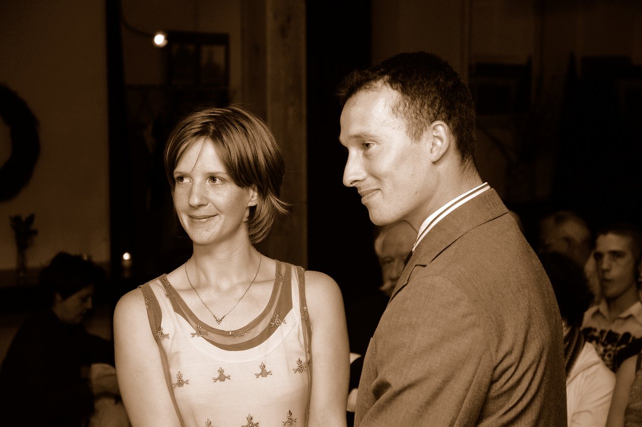 A couple stands together, smiling and looking off to the side at their wedding celebration.