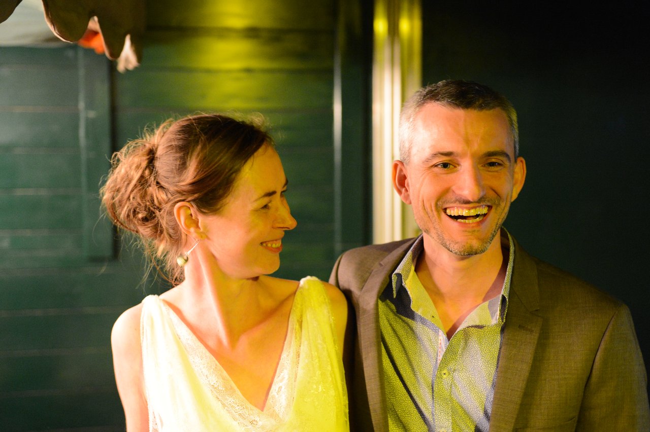 A smiling bride and groom stand together, looking happy at their wedding celebration.