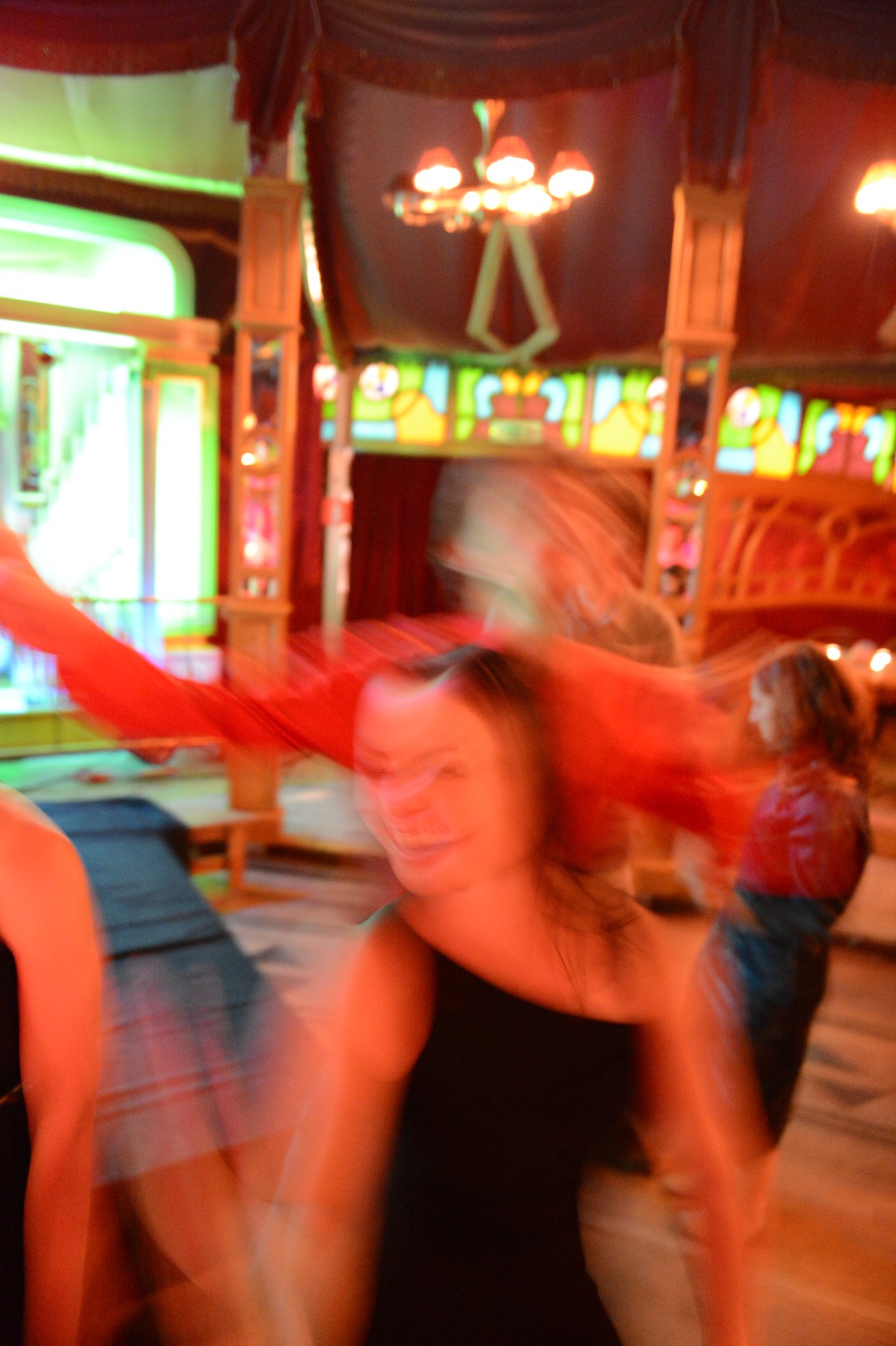 Blurred motion of people dancing at a wedding reception in a warmly lit venue with colorful stained glass.