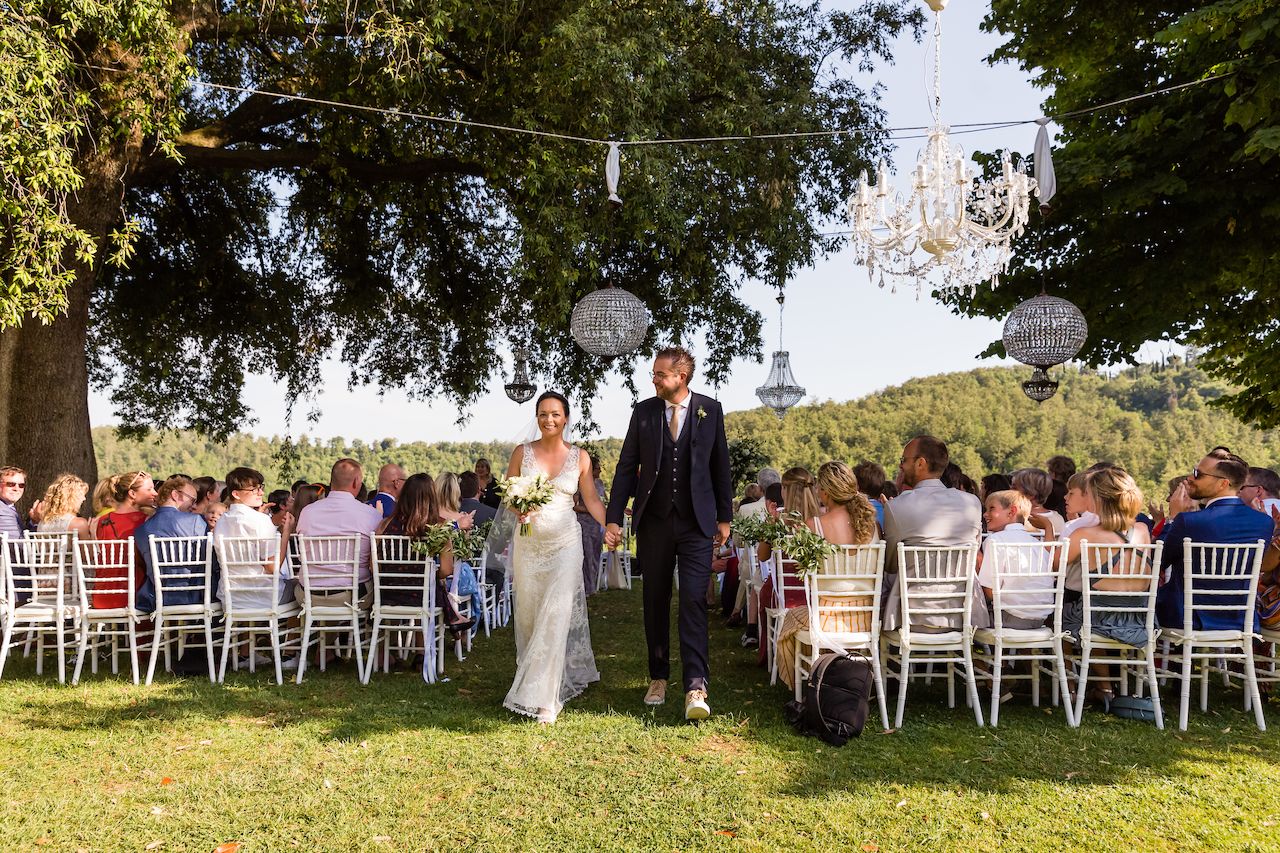 The bride and groom walk hand in hand down the aisle, smiling, as guests watch and celebrate their wedding.