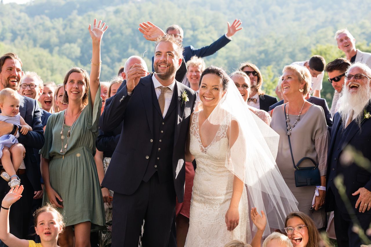 The bride and groom smile joyfully, surrounded by cheering family and friends during their wedding ceremony.