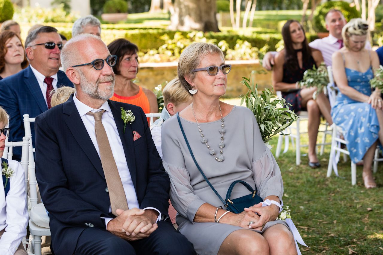 Wedding guests sit on white chairs, attentively watching the ceremony.