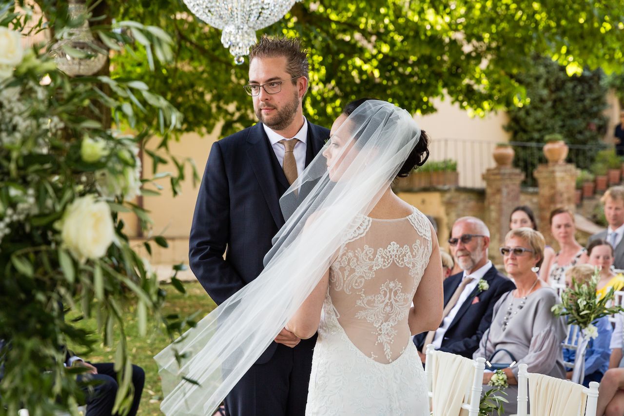 The bride and groom stand together during their wedding ceremony, with guests seated behind them.