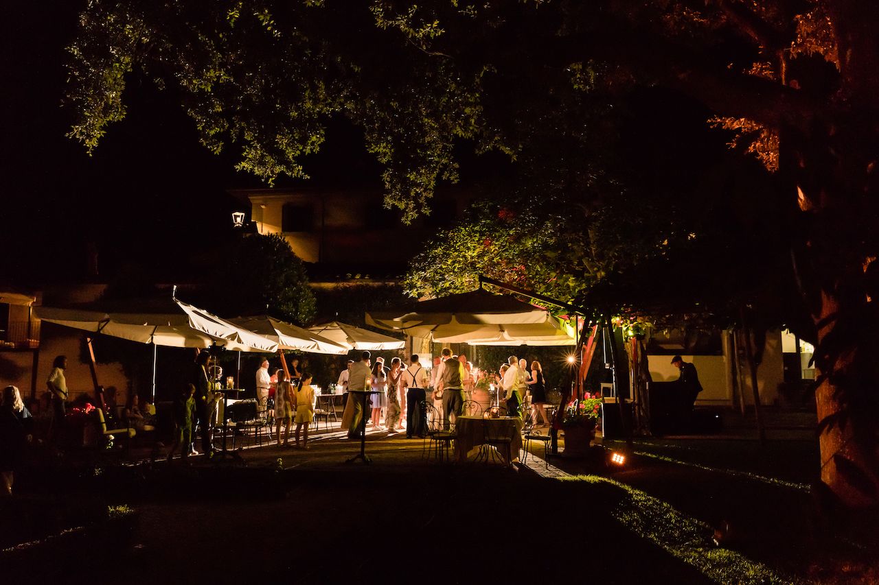 Wedding guests dancing and socializing under outdoor lights at night, with a live musician performing nearby.
