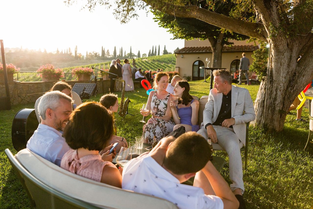 Guests sit on outdoor couches, chatting and laughing, while others stand near the bride in the background.