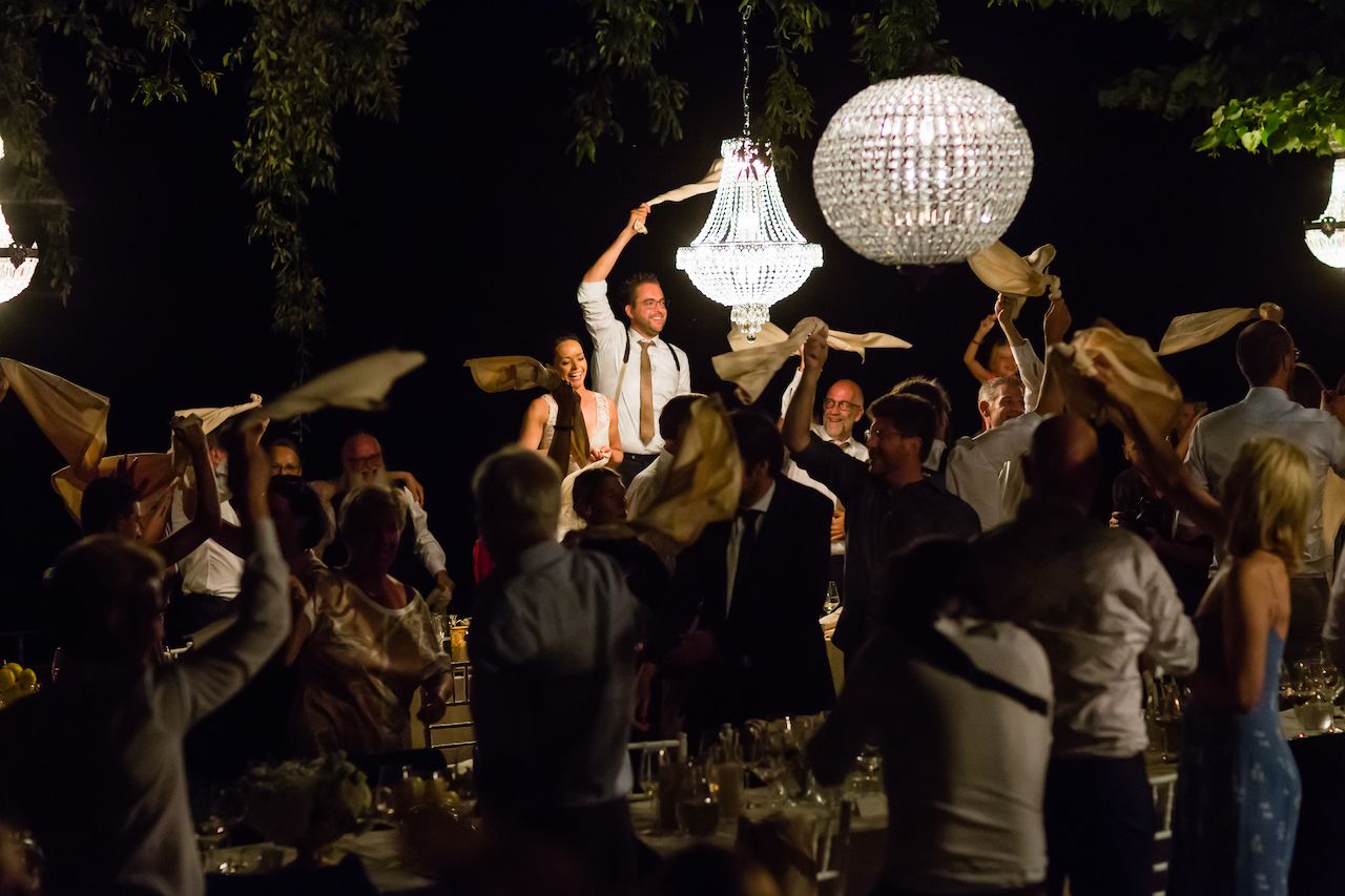 Wedding guests wave napkins in the air as the bride and groom stand and celebrate during dinner.