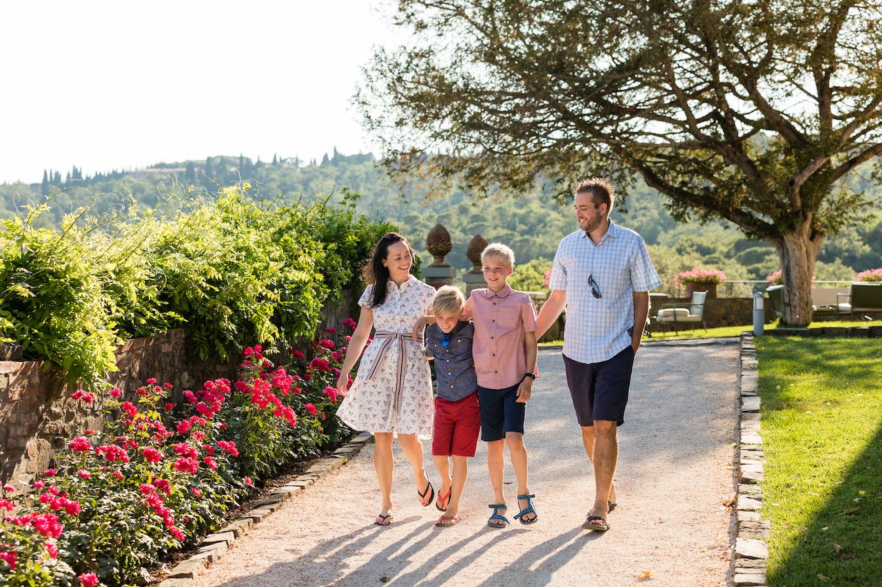 A family of four walks together on a garden path, smiling and holding hands.