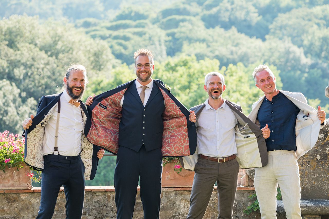 Four men stand together, smiling and holding open their suit jackets to reveal colorful linings.