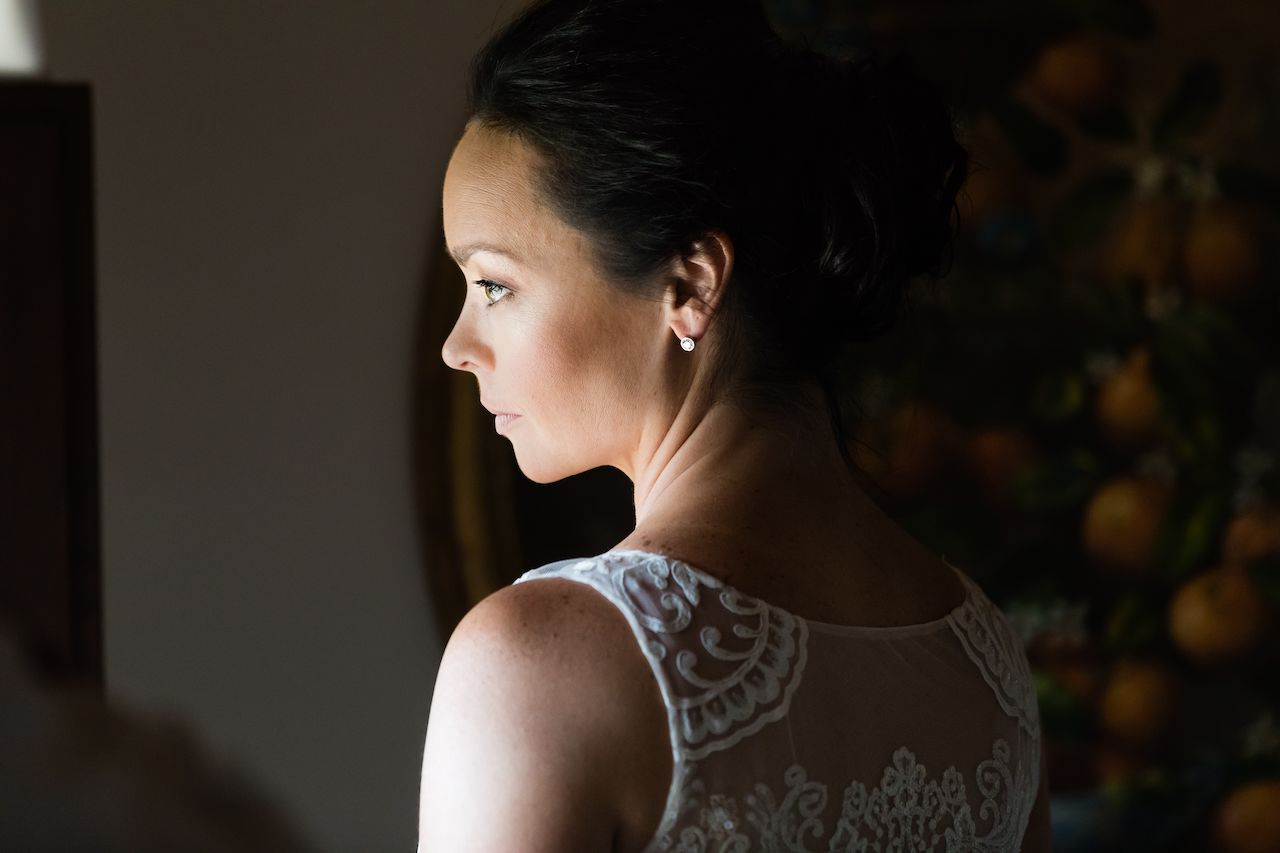 A bride in a lace dress looks to the side while getting ready for the wedding.