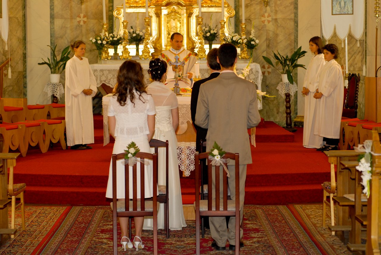 A bride and groom stand before a priest at the altar during their wedding ceremony in a church.
