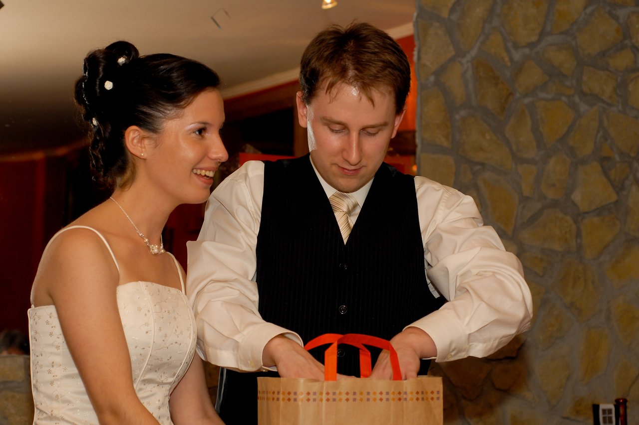 The bride smiles while the groom looks into a gift bag at their wedding reception.