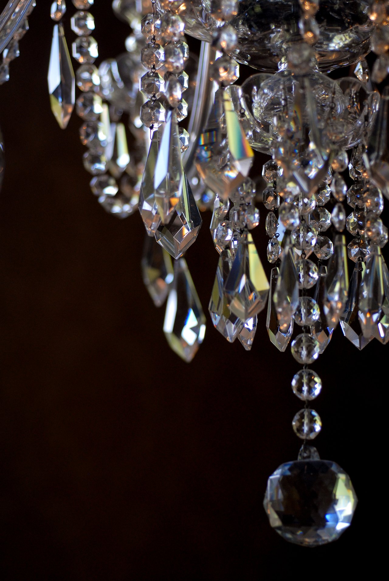Close-up of a crystal chandelier with hanging glass ornaments reflecting light against a dark background.