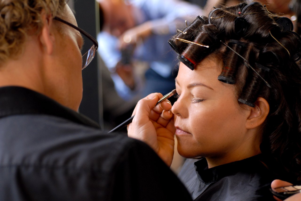 A makeup artist applies eyeshadow to a woman with hair rollers as she prepares for a wedding.