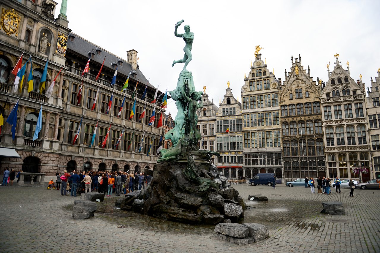 A group of people gathers near a historic fountain in a European square, possibly for a wedding celebration.