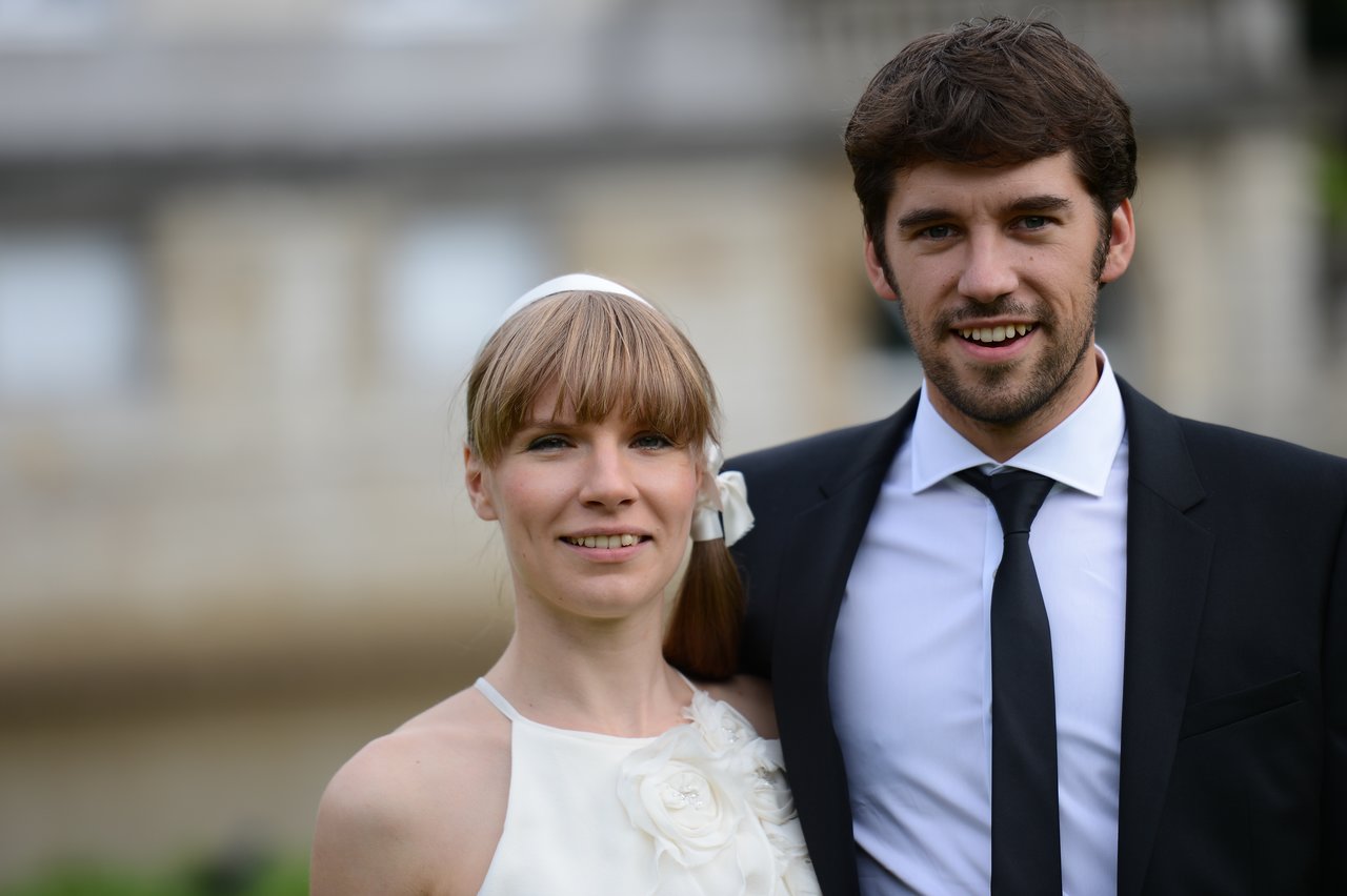 A bride and groom stand together, smiling at the camera on their wedding day.