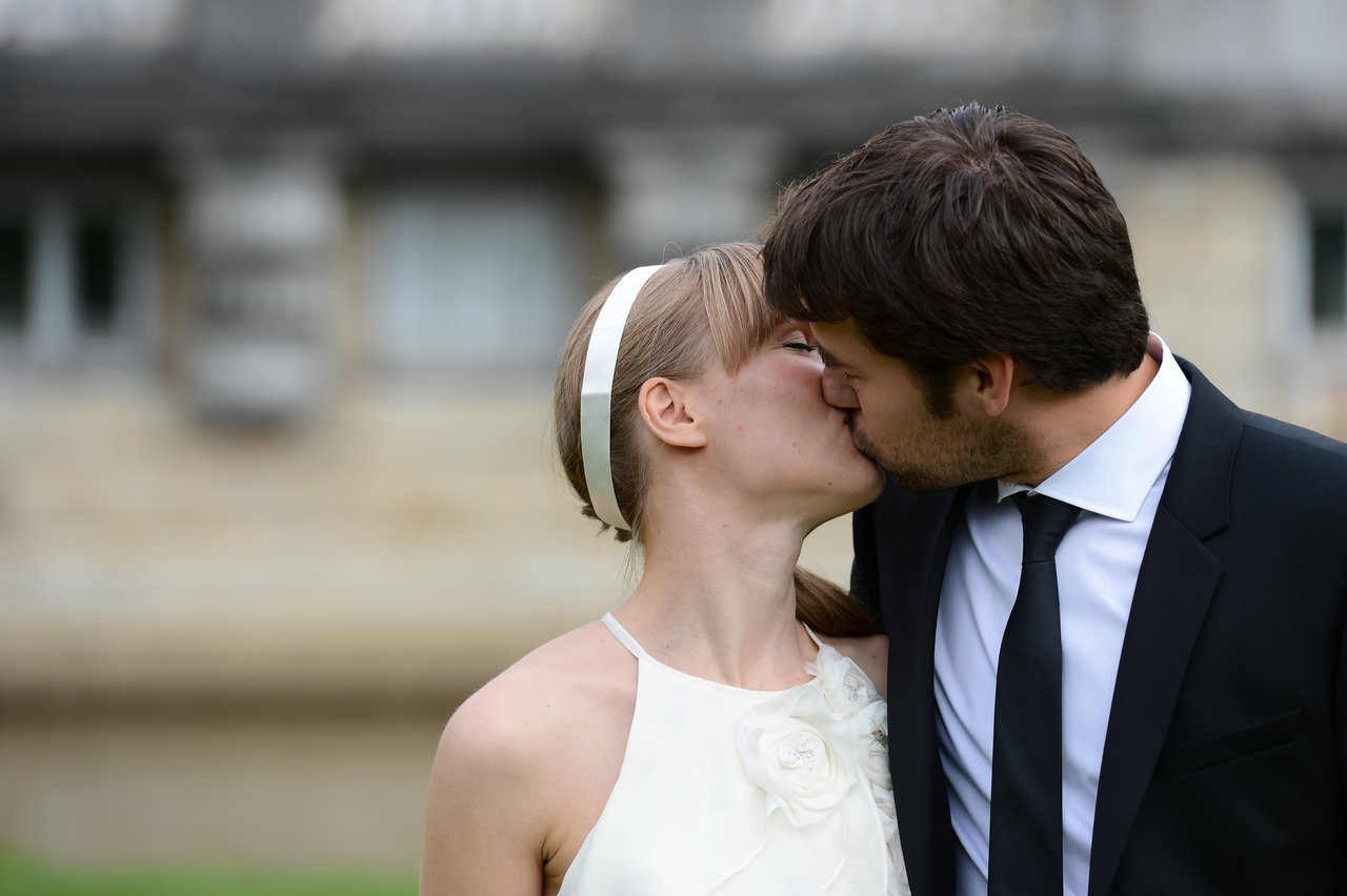 A bride and groom share a kiss outdoors on their wedding day.