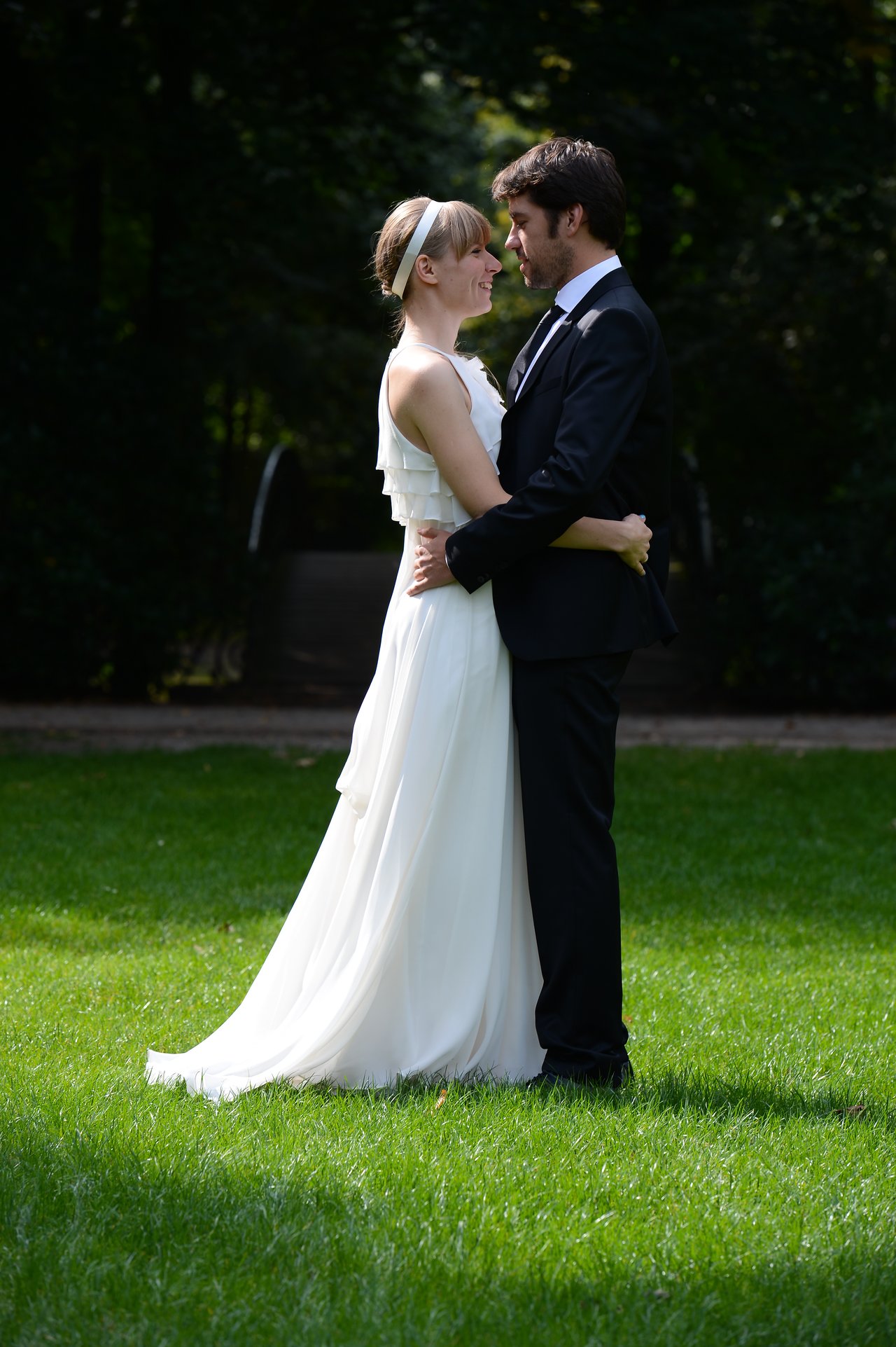 A bride and groom stand on grass, holding each other closely and smiling on their wedding day.