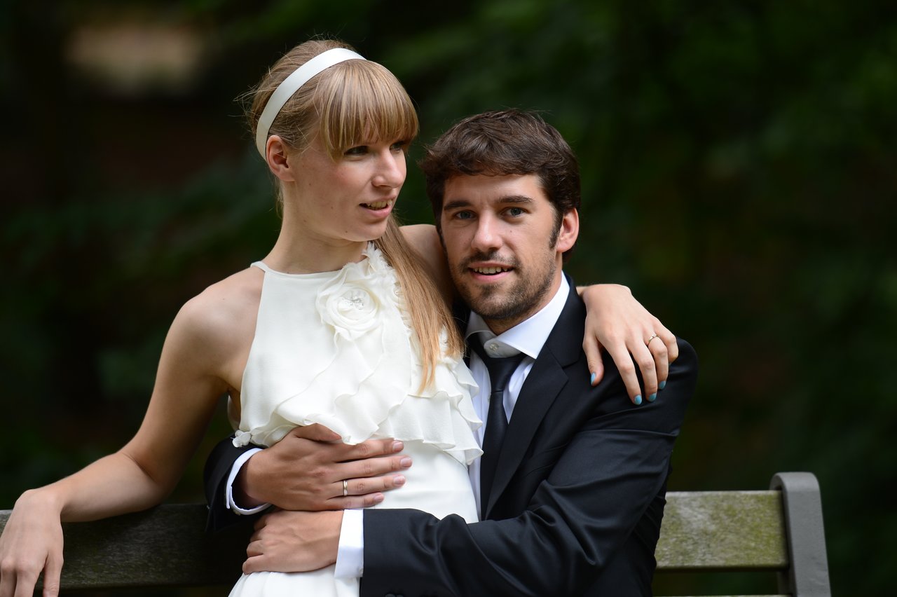 A newlywed couple sits on a bench, embracing and smiling.