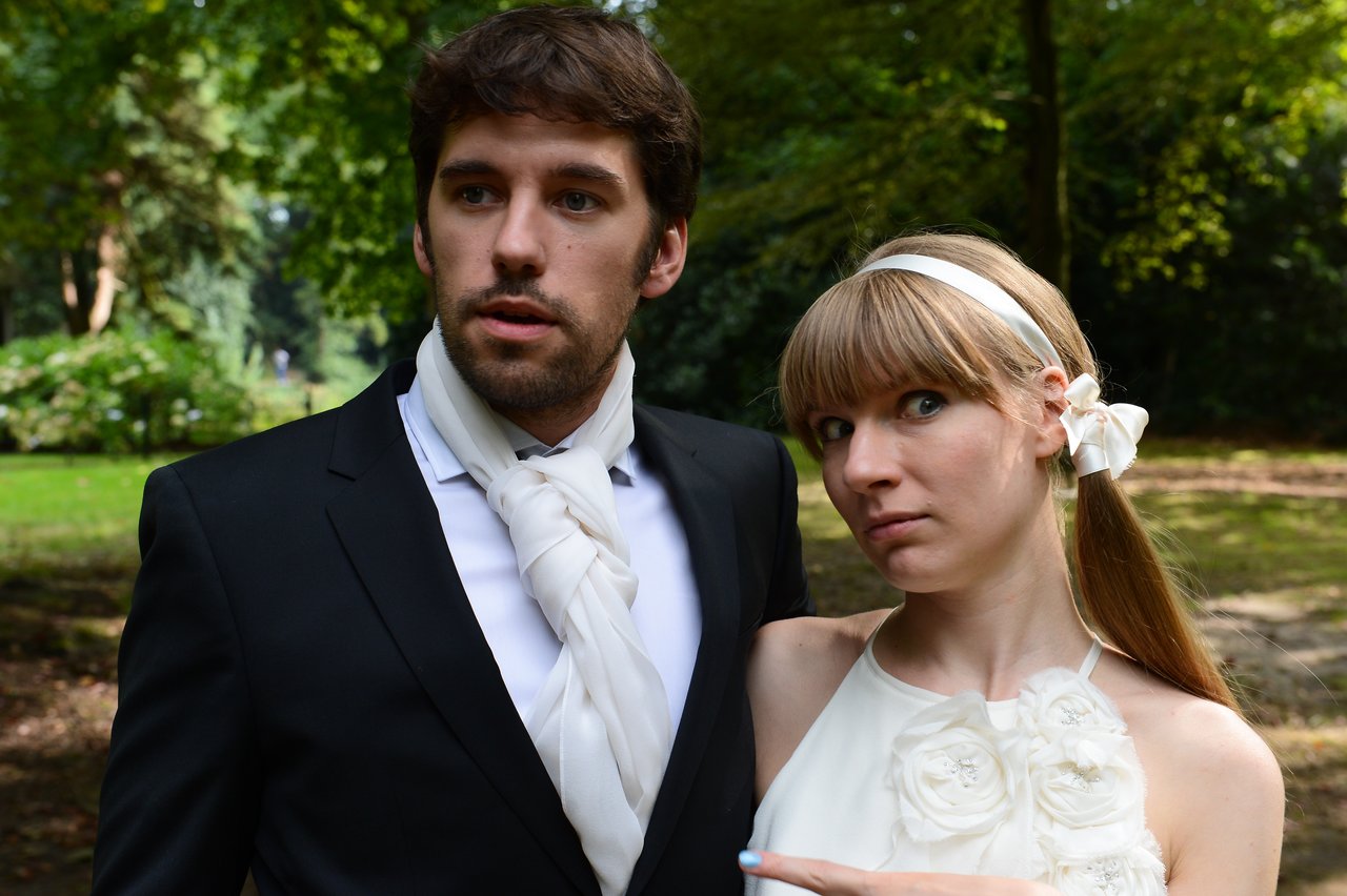 A newlywed couple poses outdoors, with the bride playfully pointing at the groom.
