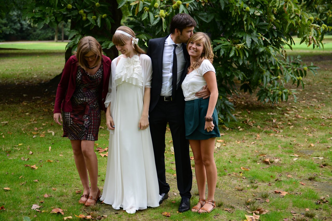 A bride in a white dress stands with three others, including a groom in a suit embracing a smiling woman.