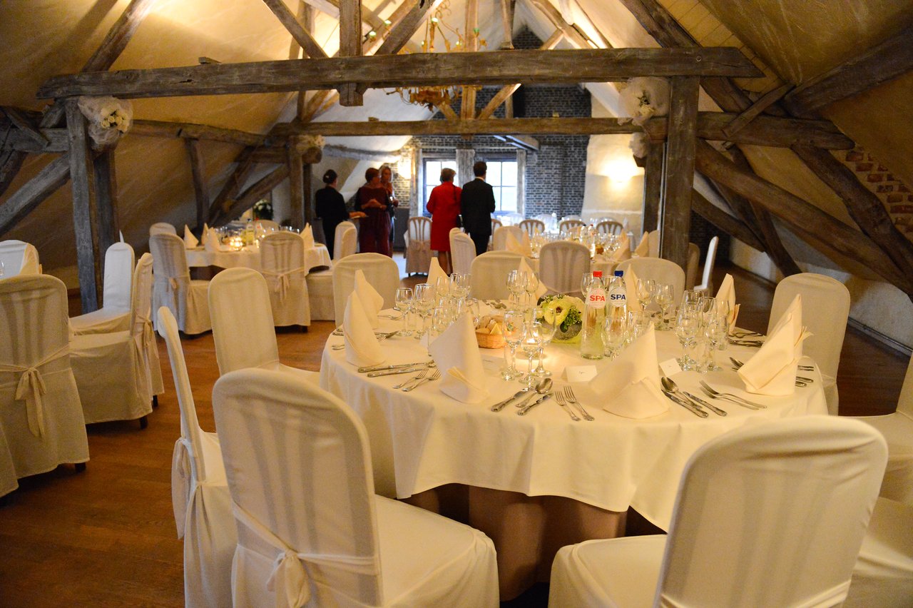 A wedding reception hall with decorated tables and guests standing in the background, engaged in conversation.